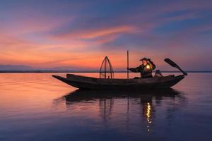 pescador asiático com barco de madeira no rio da natureza no início durante o nascer do sol foto