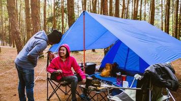 jovem casal asiático de feliz curtindo acampar na floresta de pinheiros sentar e comer na página de acampamento no meio da natureza. foto