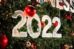 feliz ano novo 2022 brilhando na árvore de natal e bolas de enfeite foto