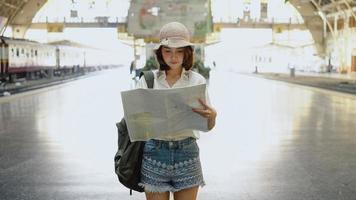 viajante mochileiro mulher asiática viajar em bangkok, Tailândia. feliz direção feminina jovem e olhando no mapa de localização na estação de trem antes da viagem. foto