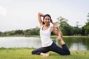jovem mulher asiática ioga ao ar livre, mantenha a calma e medite enquanto pratica ioga para explorar a paz interior. ioga tem bons benefícios para a saúde perto do lago no parque. esporte e conceito de estilo de vida saudável.