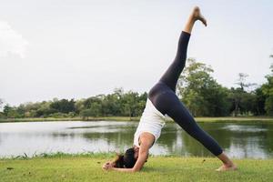 jovem mulher asiática ioga ao ar livre, mantenha a calma e medite enquanto pratica ioga para explorar a paz interior. ioga tem bons benefícios para a saúde perto do lago no parque. esporte e conceito de estilo de vida saudável.