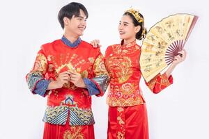 ano novo chinês, homem e mulher usam cheongsam sorrindo para dar as boas-vindas à coisa boa com dinheiro de presente e leque foto