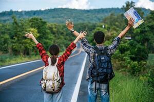 turistas homens e mulheres carregam uma mochila, ficam na estrada e levantam as mãos dos dois lados. foto
