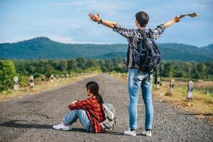 os dois turistas do sexo masculino se levantam e erguem as mãos dos dois lados. turistas femininas sentadas na rua foto