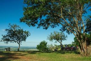 várias motos estacionadas à sombra das árvores, no topo de uma colina coberta por prados verdes e dia de sol perto do pardinho. uma pequena aldeia rural no interior do estado de são paulo. foto