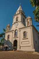 fachada de igreja e campanário em frente a uma pequena praça de paralelepípedos com jardim perene, em um dia de sol em são manuel. uma linda cidadezinha no interior do estado de são paulo. sudeste do brasil. foto