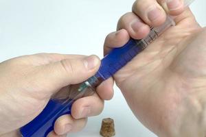 mão segurando o tubo de ensaio com um líquido azul e uma seringa. foto