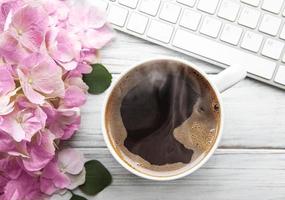 escritório em casa área de trabalho de mesa com buquê de flores de hortênsia rosa, xícara de café e teclado foto
