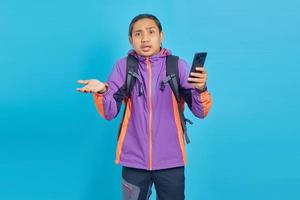 retrato de jovem asiático surpreso segurando um telefone celular com a boca aberta, isolada sobre fundo azul foto