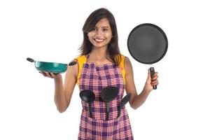 jovem mulher indiana segurando uma colher de utensílio de cozinha, estápula, concha e panela, etc. em um fundo branco foto