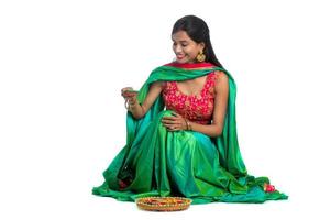 retrato de uma garota indiana tradicional segurando diya e fazendo rangoli. menina comemorando diwali ou deepavali segurando uma lâmpada de óleo durante o festival de luz sobre fundo branco foto