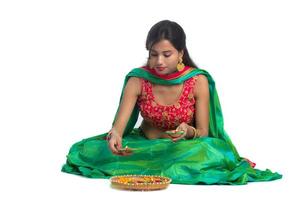 retrato de uma garota indiana tradicional segurando diya e fazendo rangoli. menina comemorando diwali ou deepavali segurando uma lâmpada de óleo durante o festival de luz sobre fundo branco foto