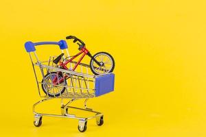 carrinho de compras de brinquedo de bicicleta pequena contra fundo amarelo foto