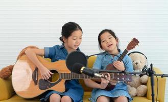 Irmãs mais velhas e mais novas, crianças cantando músicas enquanto tocam violão e ukulele juntas foto