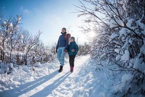 uma criança com uma mochila caminha com a mãe em um bosque nevado foto