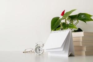 simulação de calendário em espiral em branco com folhas viradas na mesa branca com pilha de livros, óculos e relógio foto