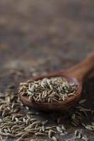 sementes de cominho em colher de pau em um plano de fundo texturizado foto