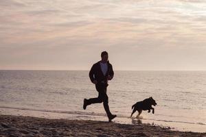 jovem caminhando na praia de manhã com cachorro preto foto