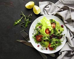 saladeira mista verde fresca com tomates e microgreens em fundo preto de concreto. alimentação saudável, vista superior. foto
