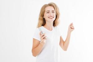 jovem mulher bonita em t-shirt usando seu smartphone isolado no fundo branco. garota loira sexy conversando com um amigo ou fazendo compras online. copie o espaço foto