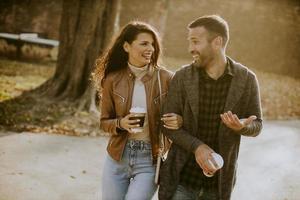 jovem casal caminhando no parque outono com café para levar xícaras nas mãos