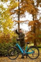 jovem bonito com bicicleta elétrica no parque outono foto
