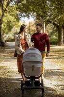 pais jovens felizes andando no parque e dirigindo um bebê no carrinho de bebê foto