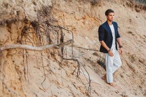 homem bonito com roupas elegantes fica no fundo de areia. lugar para texto ou publicidade foto