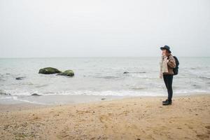 linda mulher ruiva com um chapéu e um lenço com uma mochila na costa no contexto das rochas contra o lindo mar foto