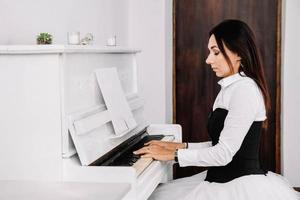 linda mulher vestida de camisa branca, tocando piano branco. lugar para texto ou publicidade