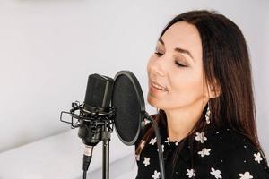 retrato de uma linda mulher canta uma música perto de um microfone em um estúdio de gravação. lugar para texto ou publicidade foto