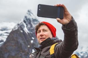 retrato de um homem viajante tirando auto-retrato com um smartphone no contexto de montanhas nevadas e rochas. lugar para texto ou publicidade