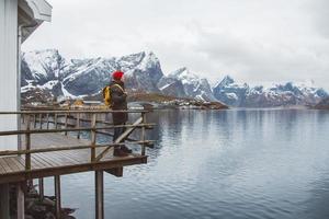jovem com uma mochila de pé em um píer de madeira, ao fundo do lago e montanhas nevadas. lugar para texto ou publicidade foto