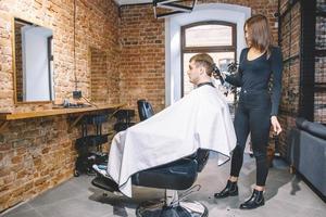 cabeleireira corta o cabelo da cabeça da cliente com aparador elétrico em barbearia