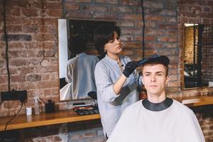 cabeleireiro de mulher bonita fazendo corte de cabelo de jovem na barbearia. conceito de publicidade e barbearia foto