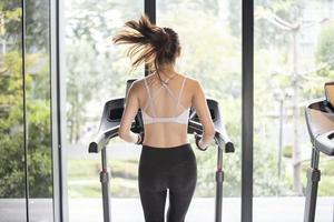 mulher bonita do esporte asiático está correndo na esteira no ginásio foto