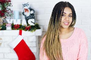 linda garota afro-americana de natal senta-se em um fundo de decorações de natal. foto