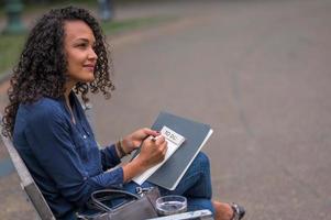 mulher negra com esmalte vermelho refletindo sua resolução de ano novo em um caderno de lista de tarefas com uma caneta preta foto