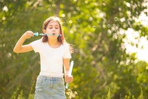 garota em uma camiseta branca. adolescente com bolhas de sabão na natureza. foto