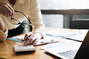 close-up mulher de negócios usando calculadora e laptop para fazer finanças matemáticas na mesa de madeira no escritório e negócios trabalhando fundo, impostos, contabilidade, estatísticas e conceito de pesquisa analítica foto