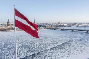 panorama da cidade de riga com uma grande bandeira letã em primeiro plano durante o dia ensolarado de inverno. foto