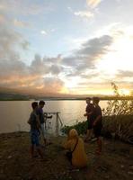 indonésia, julho de 2021 - um grupo de jovens apreciando o pôr do sol na beira do lago