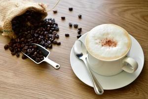 café quente da manhã para quem gosta de beber café e grãos de café torrados em um saco derramado em um piso de madeira para moer e preparar para beber na hora. foto