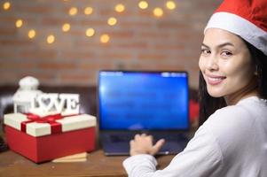 jovem sorridente usando chapéu de papai noel vermelho fazendo videochamada na rede social com a família e amigos no dia de natal.