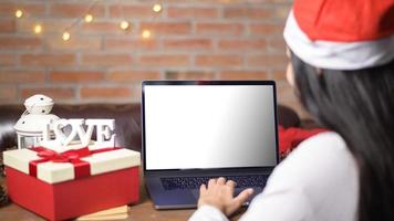 jovem sorridente usando chapéu vermelho de papai noel fazendo videochamada na rede social com familiares e amigos no dia de natal. maquete da tela do monitor do laptop. foto