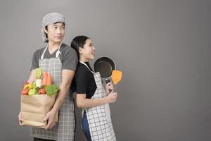 casal feliz está segurando legumes na sacola de compras em fundo cinza de estúdio foto