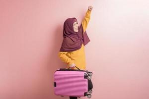 mulher muçulmana com hijab está segurando bagagem em fundo rosa, conceito de viagem de pessoas foto