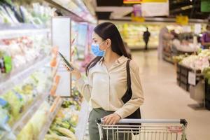 mulher está fazendo compras no supermercado com máscara facial foto