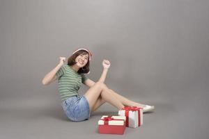 retrato de mulher bonita com chapéu de papai noel vermelho segurando a caixa de presente sobre fundo de estúdio, natal e ano novo conceito foto